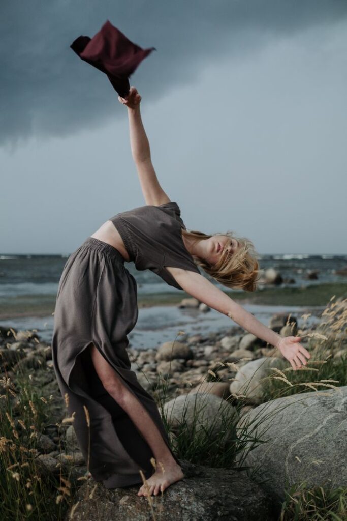 A dancer elegantly poses on rocky terrain near the sea, capturing the essence of movement and nature.