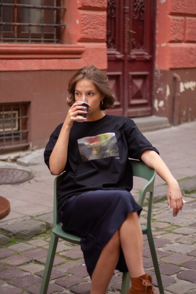 A young woman sipping coffee while seated on an urban street, capturing a moment of relaxation.