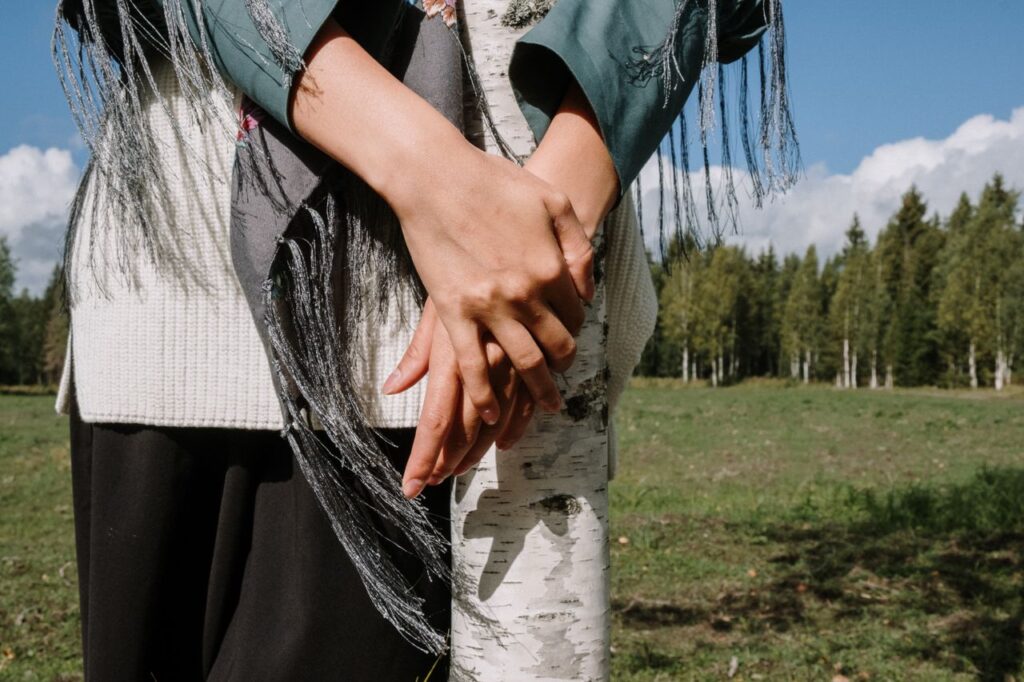 Close-up of a woman with crossed hands around a birch tree in nature.