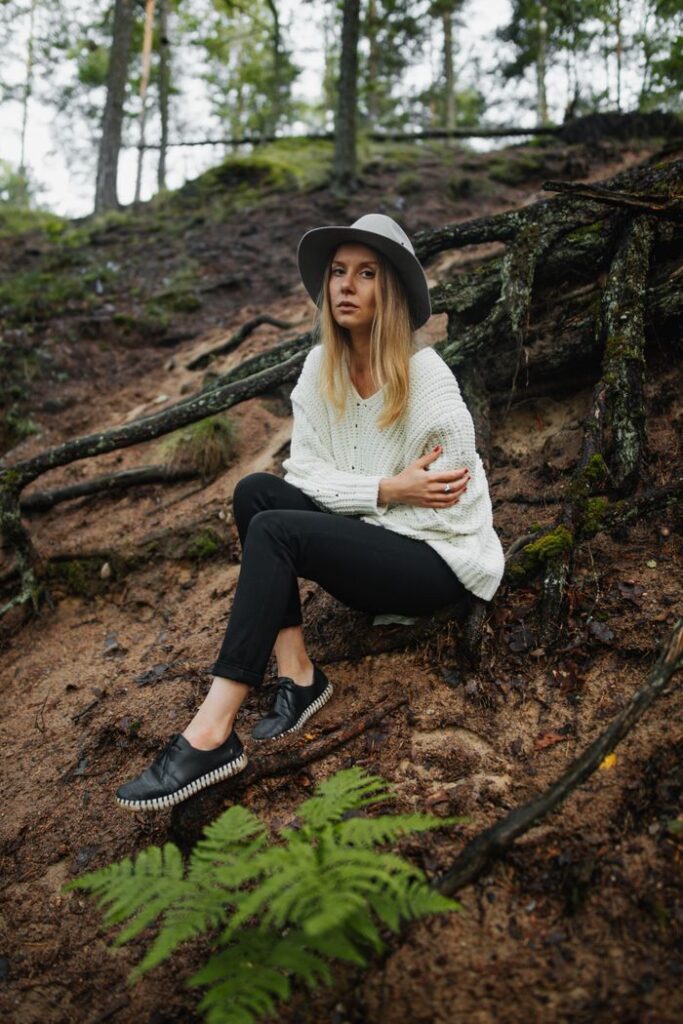 Woman in forest with knitted sweater and hat sitting on earthy ground.